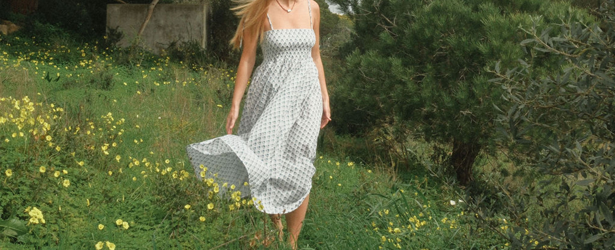 woman in white floral sundress walking in field of green grass