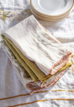 A stack of our napkins sitting on a table covered with a white linen tablecloth.