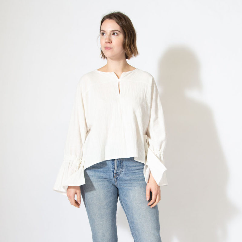 Front view of straight size model wearing white long sleeve with bell sleeves.