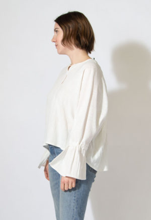 Side view of straight size model wearing white long sleeve with bell sleeves.