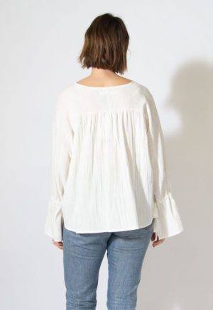 Back view of straight size model wearing white long sleeve with bell sleeves and gathers across the back.