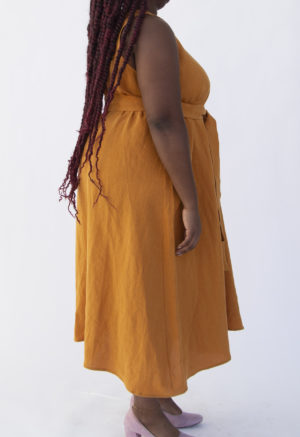 Close up side view of plus size model wearing Reversible Scoop Dress in Saffron Linen with a sash.