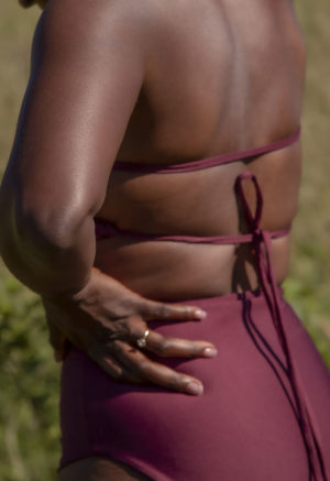 Close-up back/side view of straight size model in the Fig Halter Tie Top, standing in the tall grass.