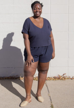 Front view of plus size model in Navy Rib Reversible Short Sleeve Top standing in front of white brick wall.