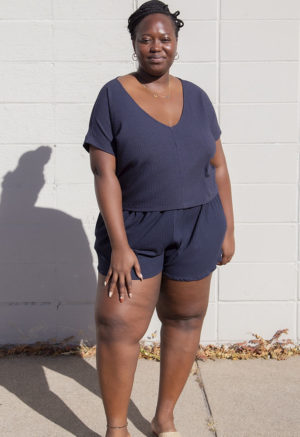 Front view of plus size model in Navy Rib Reversible Short Sleeve Top standing in front of white brick wall.