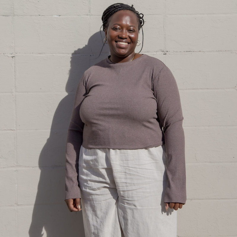 Front view of a plus size model in the Mauve Rib Cropped Long Sleeve Top, standing in front of white brick wall.