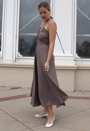 Side view of a straight size model in the Mauve Rib Everything Tank Dress, standing, standing outside in front of large windows.