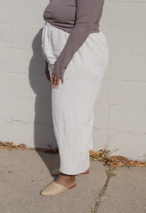 Side view of a plus size model in the Mauve Rib Cropped Long Sleeve Top, standing in front of white brick wall.