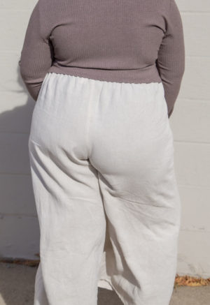 Back view of a plus size model in the Mauve Rib Cropped Long Sleeve Top, standing in front of white brick wall.