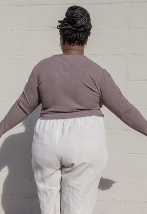 Back view of a plus size model in the Mauve Rib Cropped Long Sleeve Top, standing in front of white brick wall.