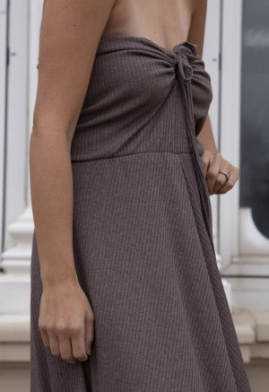 Close-up front/side view of a straight size model in the Mauve Rib Everything Tank Dress, standing, standing outside in front of large windows.