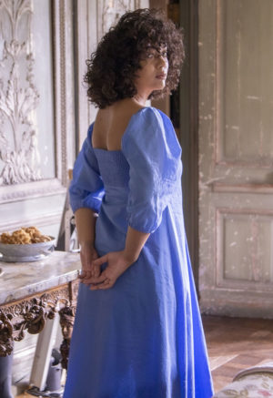 Back/side view of straight size model in Cerulean Blue Keyhole Maxi Dress standing in front of ornate table.