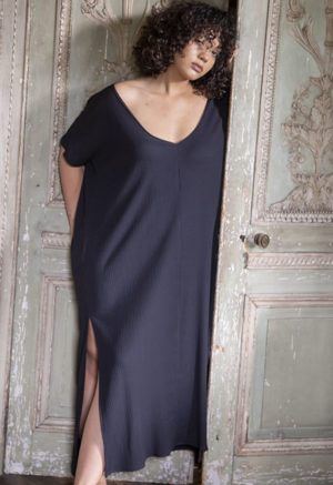Front view of a straight size model in the Navy Rib Reversible Side Slit Dress, standing in front of ornate wooden doors.