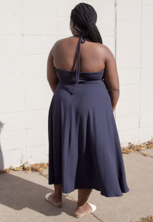 Back view of a plus size model in the Navy Rib Everything Tank Dress, standing in front of white brick wall.
