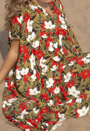 Front/side view of straight size model in Island Floral Double V Tiered Maxi Dress sitting on beach.