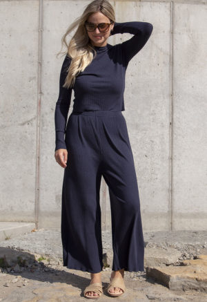 Front view of a straight size model in the Navy Rib Cropped Long Sleeve Top, standing in front of concrete wall.