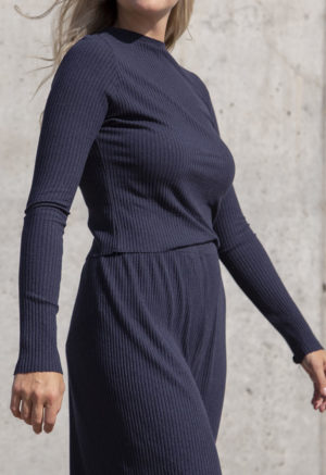 Side view of a straight size model in the Navy Rib Cropped Long Sleeve Top, standing in front of concrete wall.