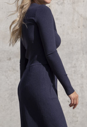 Side view of a straight size model in the Navy Rib Cropped Long Sleeve Top, standing in front of concrete wall.