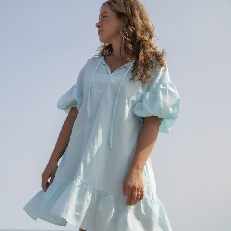 Front view of straight size model in Capri Blue Reversible Ruffle Dress standing outside.