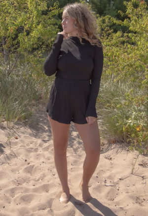 Front view of a straight size model in the Black Rib Cropped Long Sleeve Top, standing outside on beach path.