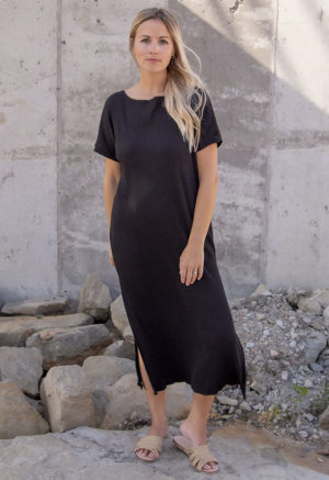 Front view of a straight size model in the Black Rib Reversible Side Slit Dress, standing in front of concrete wall.