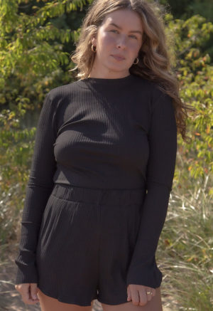 Front view of a straight size model in the Black Rib Cropped Long Sleeve Top, standing outside on with trees in background.