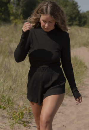 Front view of a straight size model in the Black Rib Cropped Long Sleeve Top, standing outside on beach path.