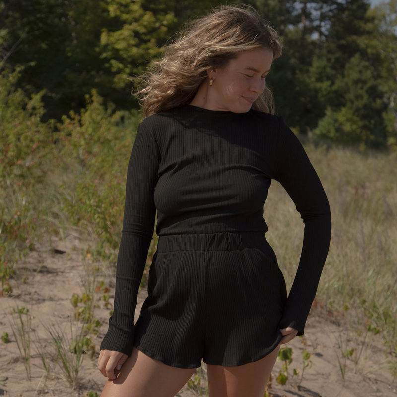 Front view of a straight size model in the Black Rib Cropped Long Sleeve Top, standing outside on grassy sand.