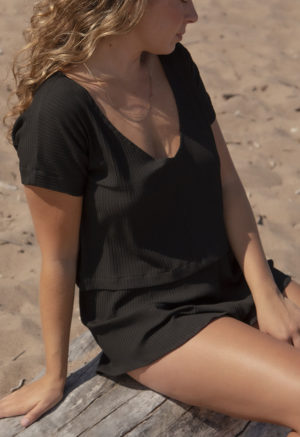 Front/side view of straight size model in Black Rib Reversible Short Sleeve Top sitting on bench on the beach.