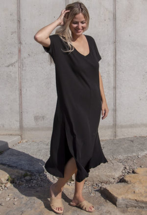 Front view of a straight size model in the Black Rib Reversible Side Slit Dress, standing in front of concrete wall.