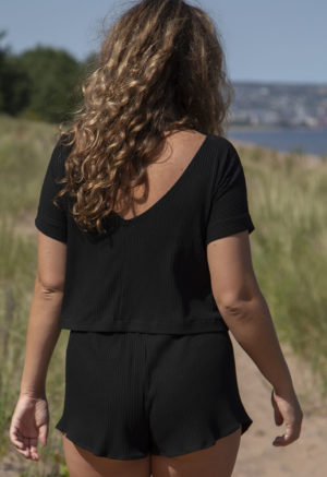 Back view of straight size model in Black Rib Reversible Short Sleeve Top standing on beach path.
