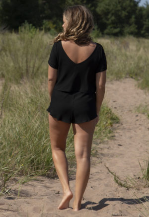 Back view of straight size model in Black Rib Reversible Short Sleeve Top standing on beach path.
