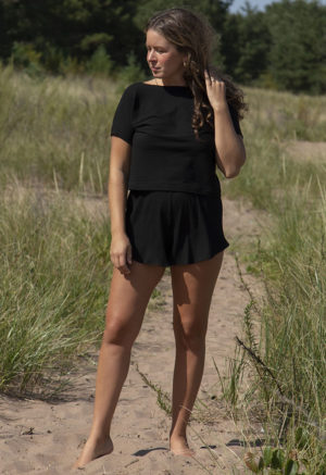 Front view of straight size model in Black Rib Reversible Short Sleeve Top standing on beach path.