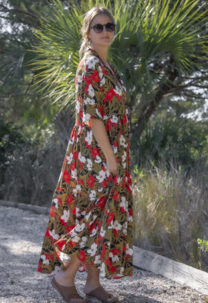 Side view of straight size model wearing Island Floral Tiered Lapel Dress standing on path with bushes behind her.