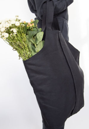 Side view of straight size model carrying Black Baguette Tote with flowers.