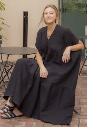 Front view of straight size model sitting and wearing Black Gauze Double V Tiered Maxi Dress.