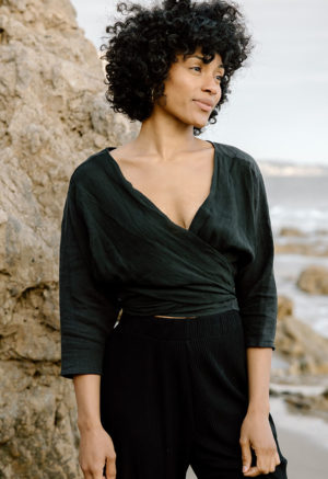 woman on beach in black long sleeve wrap top and black rib pants