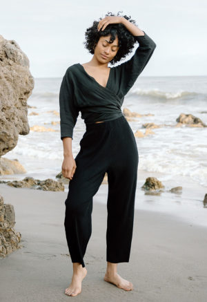 woman on beach in black long sleeve wrap top and black rib pants