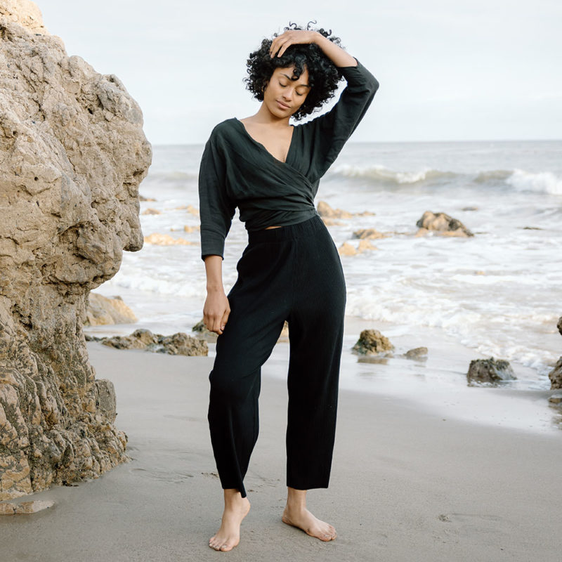 woman on beach in black long sleeve wrap top and black rib pants