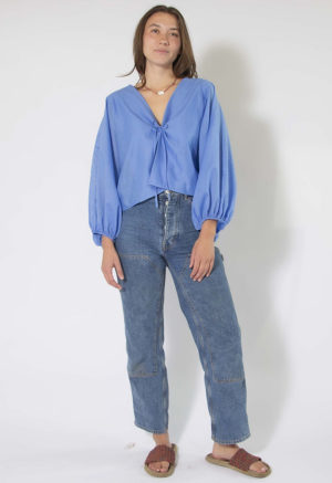 woman in cerulean blue balloon sleeve tie top and dark blue jeans