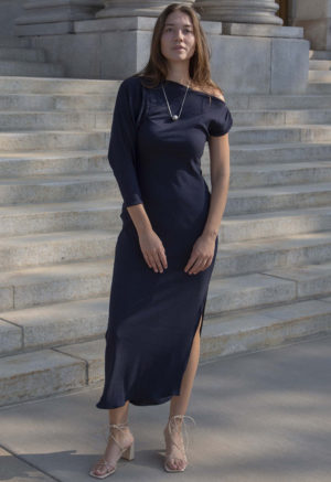 Woman in blue rib maxi length dress with an asymmetrical neck line and high slit on one side of the skirt