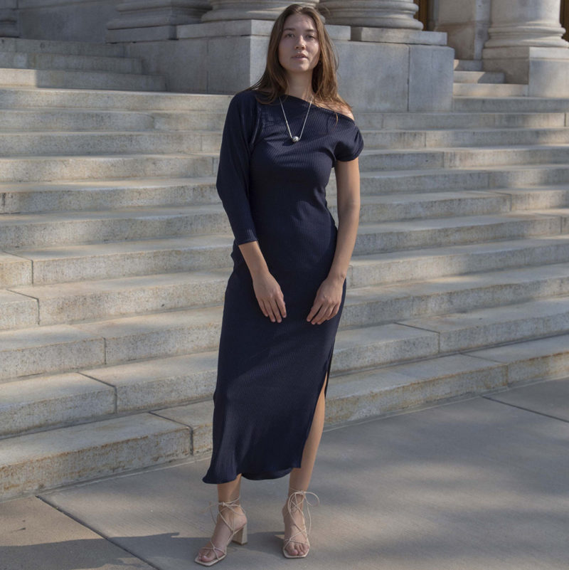 Woman in blue rib maxi length dress with an asymmetrical neck line and high slit on one side of the skirt