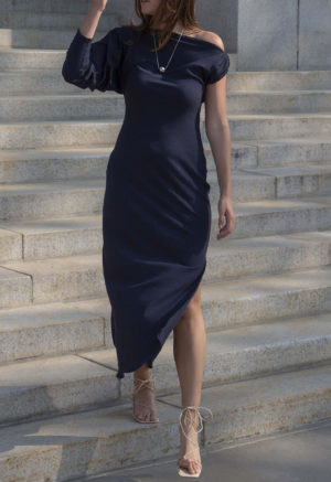 Woman in blue rib maxi length dress with an asymmetrical neck line and high slit on one side of the skirt