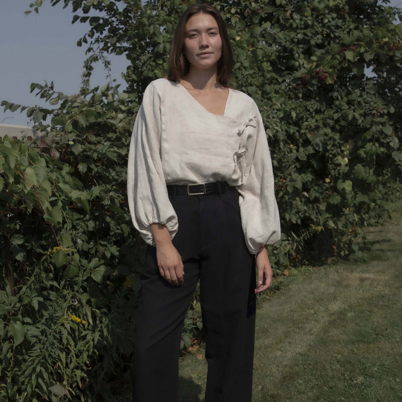 woman in oatmeal linen asymmetrical blouse with black slacks and black belt