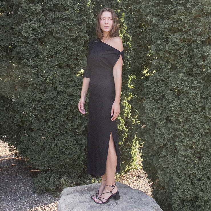 Woman in black rib maxi length dress with an asymmetrical neck line and high slit on one side of the skirt