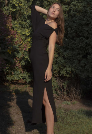 Woman in black rib maxi length dress with an asymmetrical neck line and high slit on one side of the skirt