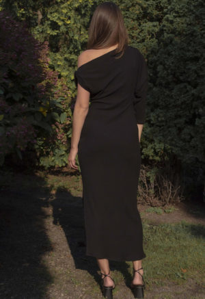 Woman in black rib maxi length dress with an asymmetrical neck line and high slit on one side of the skirt