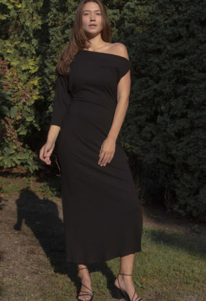 Woman in black rib maxi length dress with an asymmetrical neck line and high slit on one side of the skirt