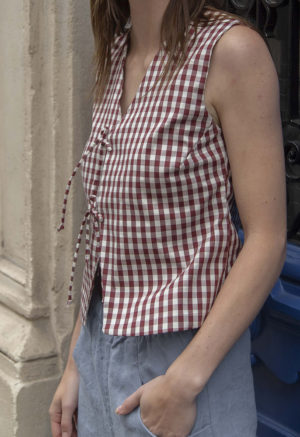 woman in dark maroon and white plaid tie vest and denim pants standing on a street