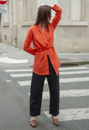 woman in bright poppy wrap blazer, black pants, brown slides standing on street